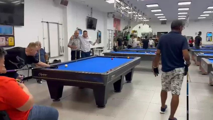 Vista de un salón con varias mesas de billar y jugadores